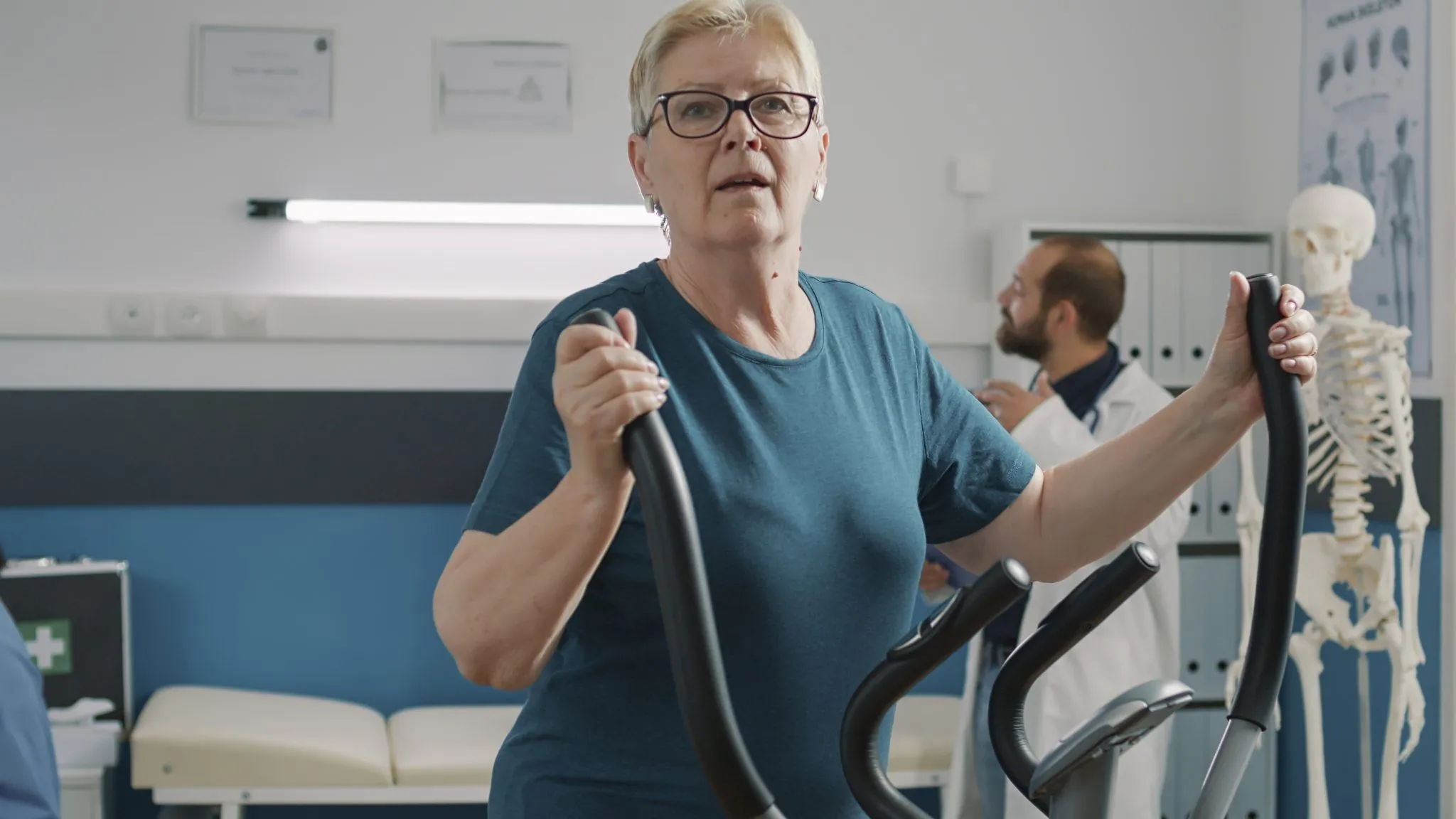 A senior woman with glasses exercises on an elliptical machine